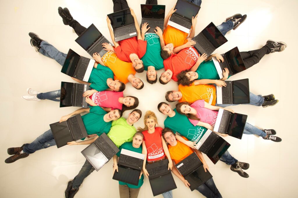 Lots of students are holding their computers and are lying down on the floor looking at the camera.