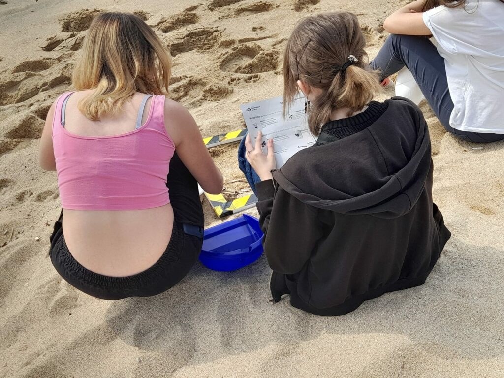 2 young students are looking at a piece of paper. They are sitting on the ebach.