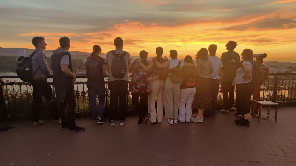 Students are giving their back to the camera and they are looking at the sunset.